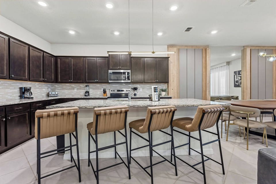Step into a stylish kitchen featuring sleek dark cabinetry and light marble countertops for a vibrant atmosphere. Comfortable bar stools invite you to enjoy casual meals, while ample lighting adds to the welcoming vibe.