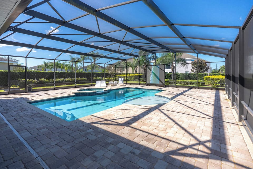 Discover your private oasis with a sparkling pool surrounded by lush greenery. Relax on the sleek paver patio and sun loungers, all within a spacious screened enclosure for comfortable outdoor enjoyment.