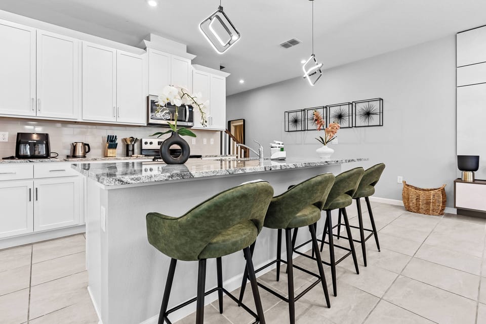 Welcome to this sleek kitchen with a spacious island and stylish green bar stools, perfect for casual meals or morning coffee. The bright cabinetry enhances the clean lines, creating an ideal space for your culinary adventures.