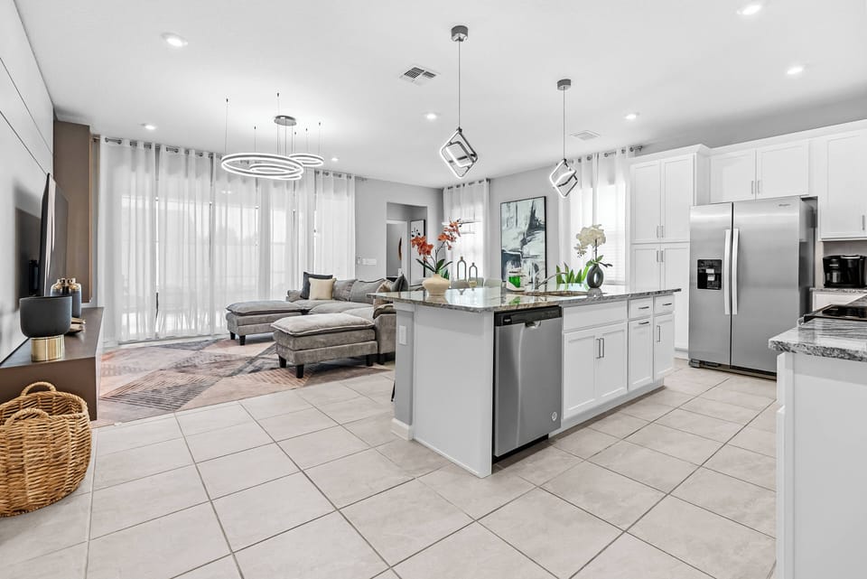 Welcome to a bright, open-concept kitchen and living area featuring sleek white cabinetry and a spacious island perfect for casual dining. Large windows illuminate the stylish decor, creating a warm and inviting atmosphere.