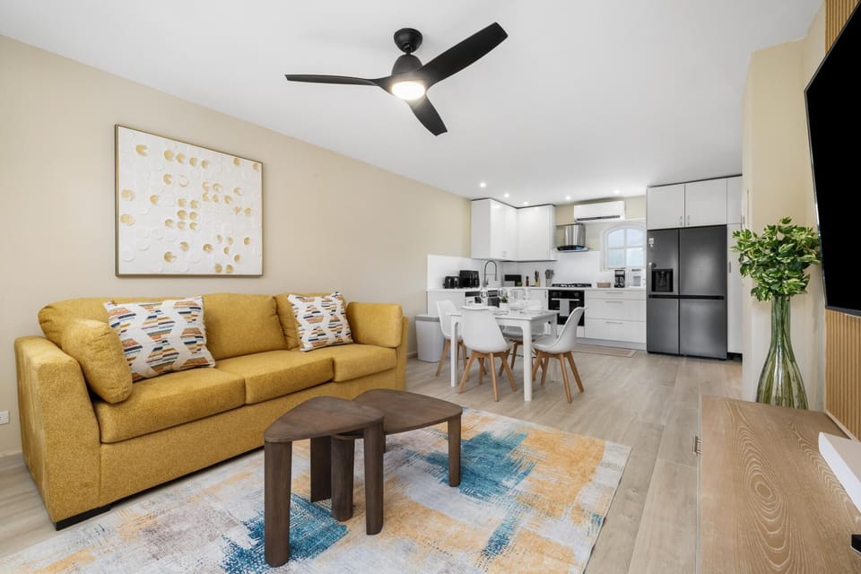 Step into a bright and airy living room with soft seating, a TV, and a warm, welcoming atmosphere. The open layout connects seamlessly to the dining area and kitchen, creating the perfect space to relax, watch a show, or share time with loved ones.