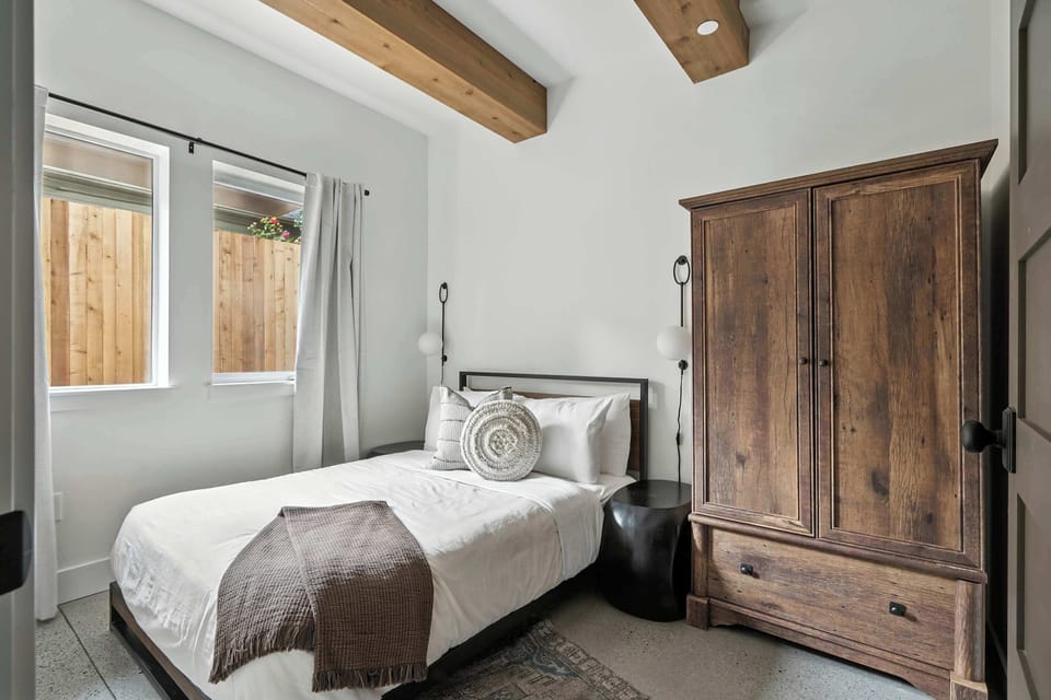Bedroom with a bed and wood armoire beneath exposed beams.