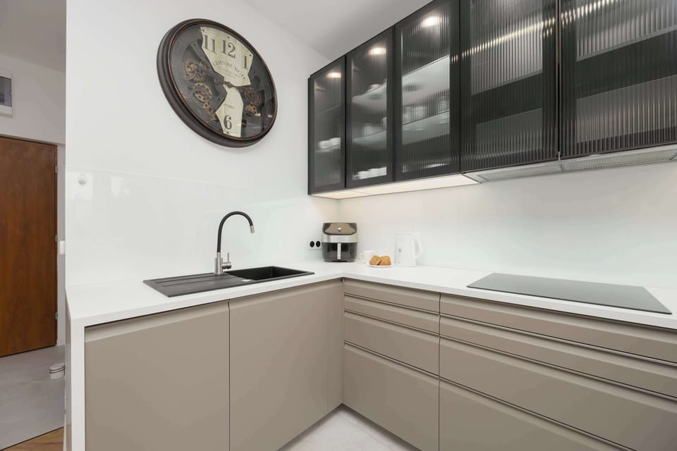 A sleek kitchen with gray cabinetry and large black-framed windows. A potted plant adds a fresh, natural accent to the clean design.