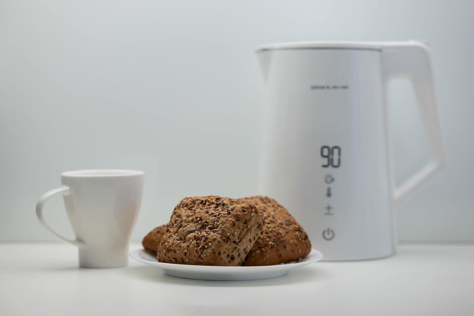 A breakfast setup with a cup, jug, and a small plate of pastries. The clean white background gives a minimalist, cozy morning vibe.