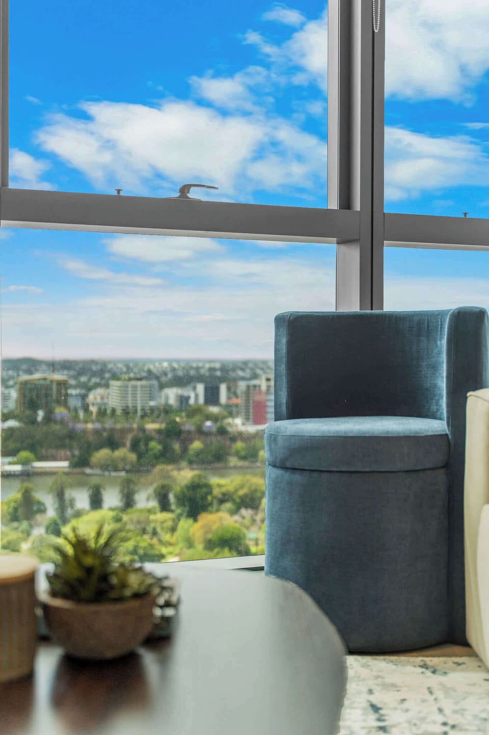 Cozy reading corner with plush blue chair and floor-to-ceiling windows overlooking the river.