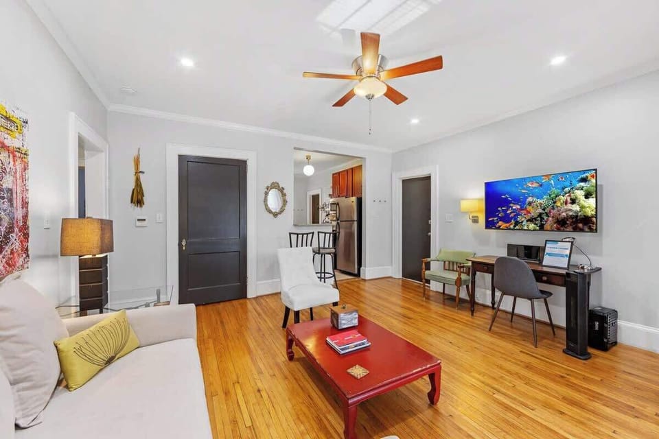 Open living area in Charlotte featuring hardwood floors, ceiling fan, mounted smart TV, and comfortable seating. Spacious layout with sleeper sofa option and dedicated desk area, ideal for relaxing or working during your stay.