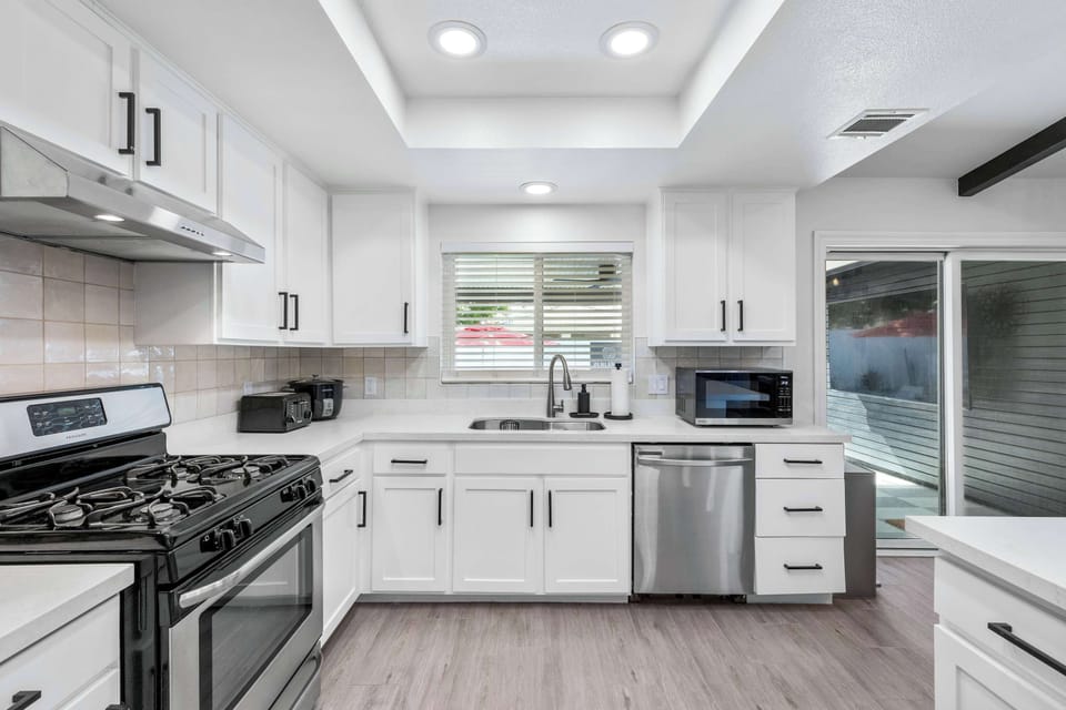 Bright kitchen with white shaker cabinets, gas range, stainless dishwasher & tile backsplash — fully loaded for group meals