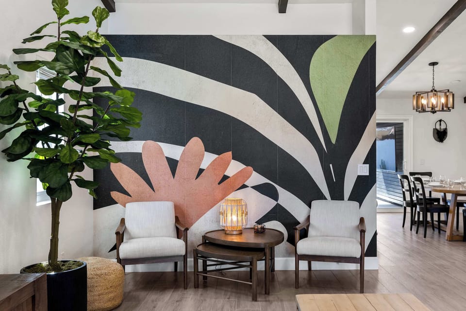 Sitting nook with floor-to-ceiling botanical mural, two linen arm chairs, and a glowing lantern table — the most Instagrammable corner in the house