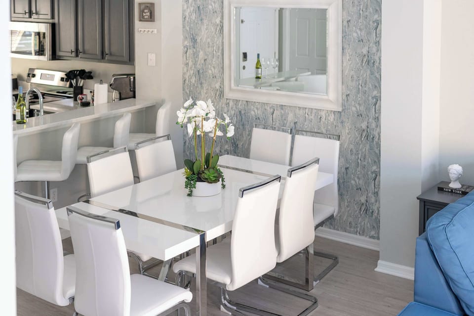 Modern dining area with white leather chairs and a sleek kitchen bar in the background