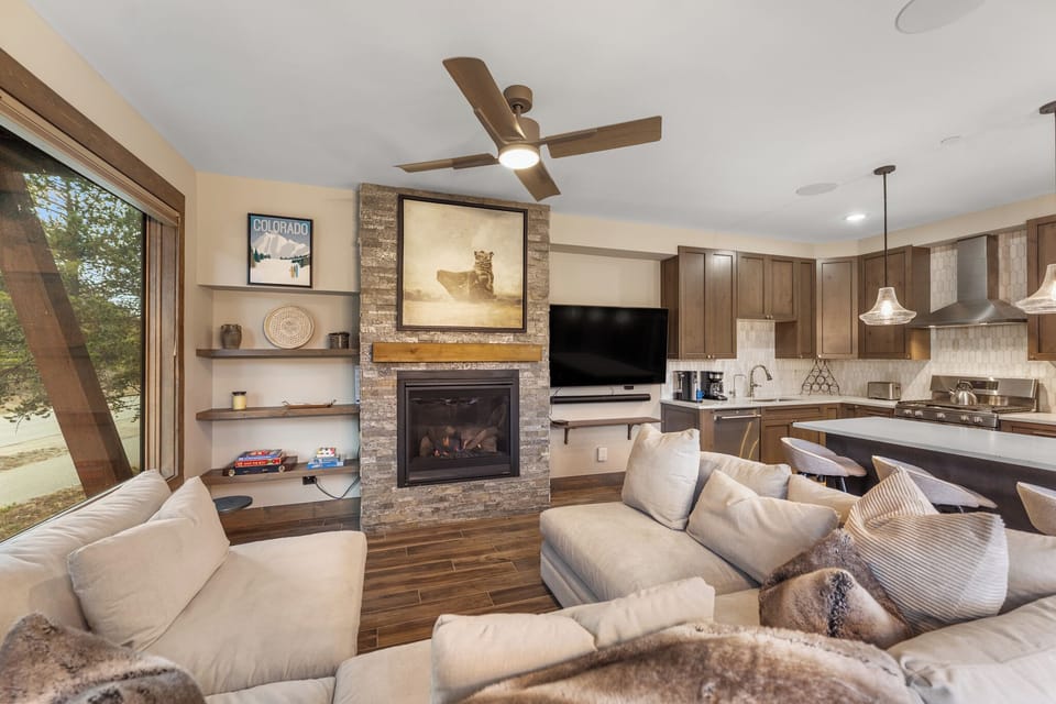 Sink into plush sofas by your stone fireplace while mountain views frame this elegant living space with modern kitchen nearby.