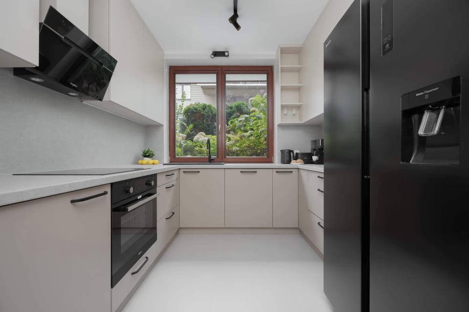 A modern kitchen with contrasting black and white finishes, high-end appliances, and a window overlooking the garden.