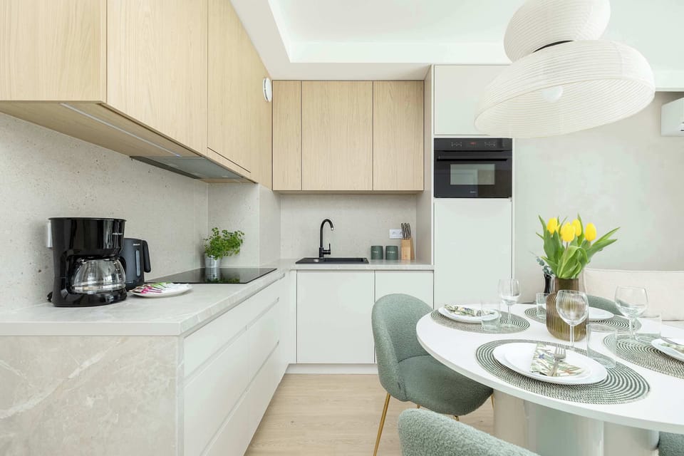 Modern kitchenette combined with a dining space for four. Clean cabinetry, built-in appliances, and soft colors create a balanced design.