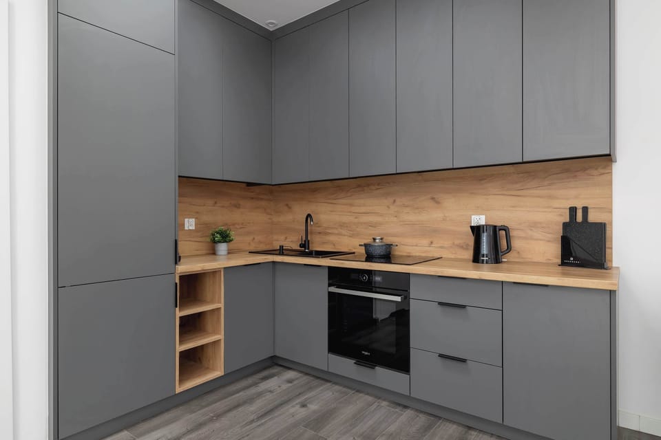 A modern kitchenette with grey cabinets and wooden countertops. It includes an induction stove, oven, and coffee maker.