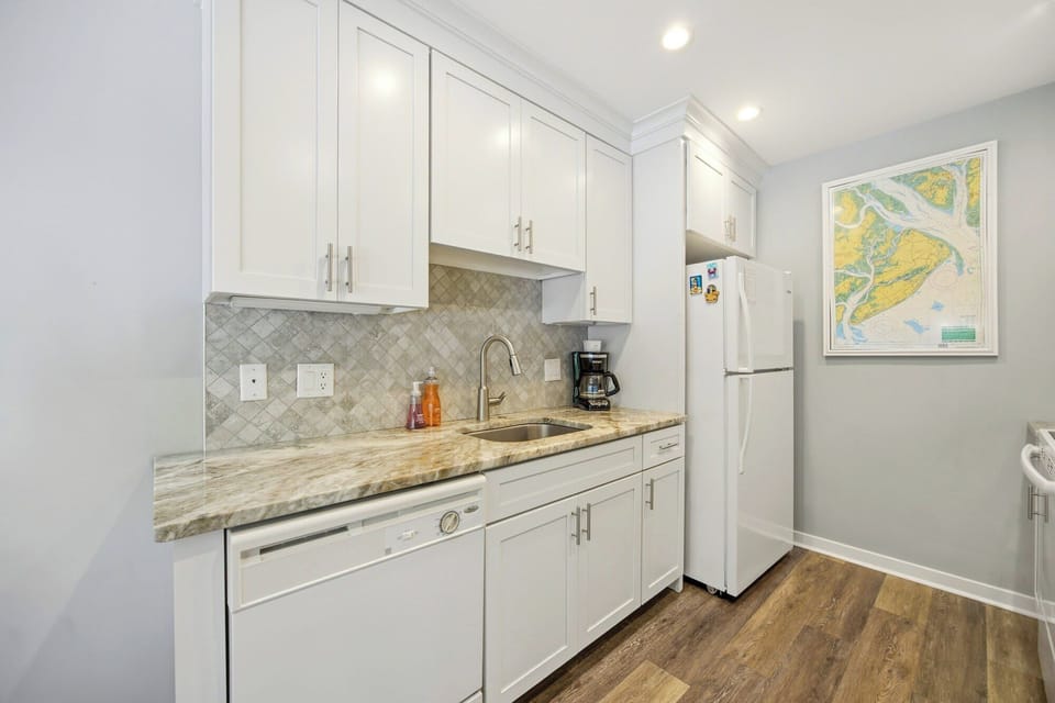 Marbled stone countertops and crisp white cabinetry create a bright, airy corner for your morning brew. Tiled textures and warm wood floors add a grounded, homey feel to this modern, efficient kitchen space.