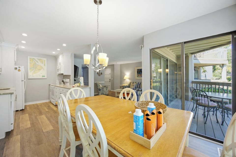 Pine wood surfaces and white lattice chairs create a cheerful hub for morning coffee and shared meals. Sliding glass doors pull in the afternoon glow, connecting this airy dining space to a quiet balcony for seamless indoor and outdoor living.