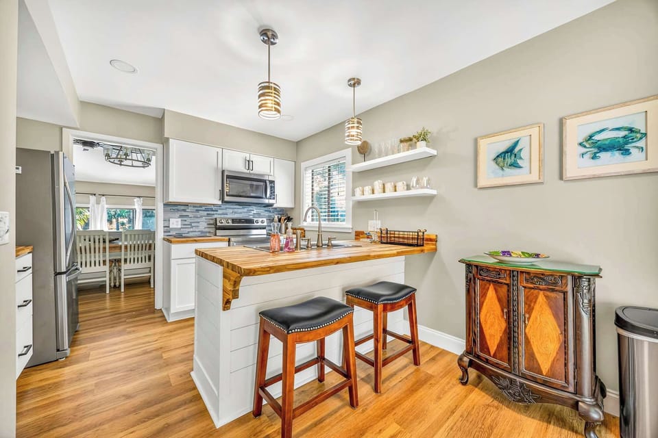 Natural wood countertops bring organic warmth to this airy kitchen, where soft pendant lighting and coastal accents create a serene hub for morning coffee. Smooth finishes and shiplap details offer a fresh, modern take on beachside living.