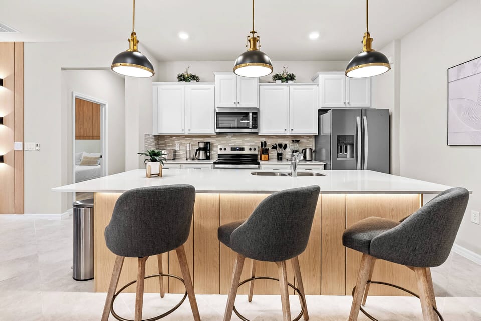 This stylish kitchen boasts sleek white cabinetry and a beautiful marble countertop, creating a bright, functional space. The upholstered bar stools invite casual gatherings, and the pendant lighting adds warmth and charm.