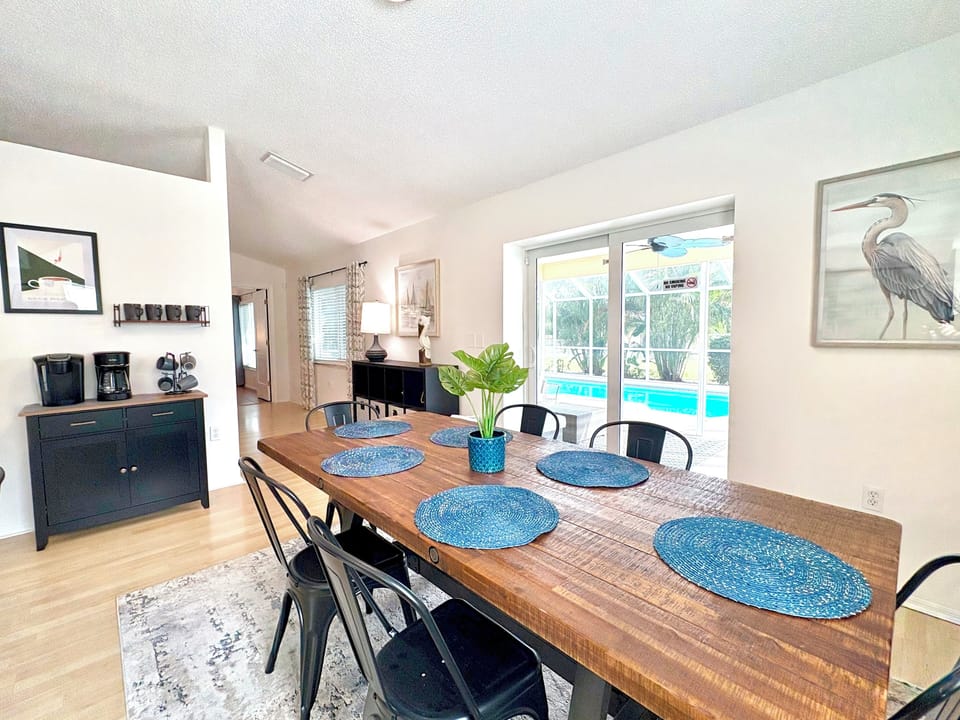 Dining table with pool view through sliding glass doors and coastal heron wall art