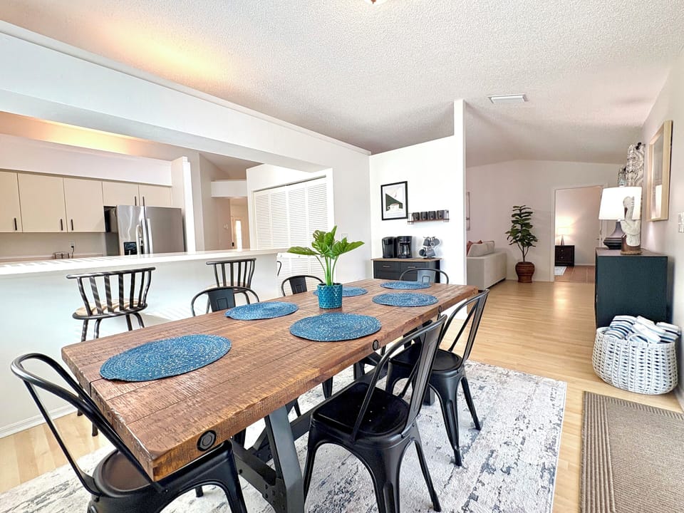 Dining area with long wooden table, metal chairs, and open floor plan with kitchen beyond