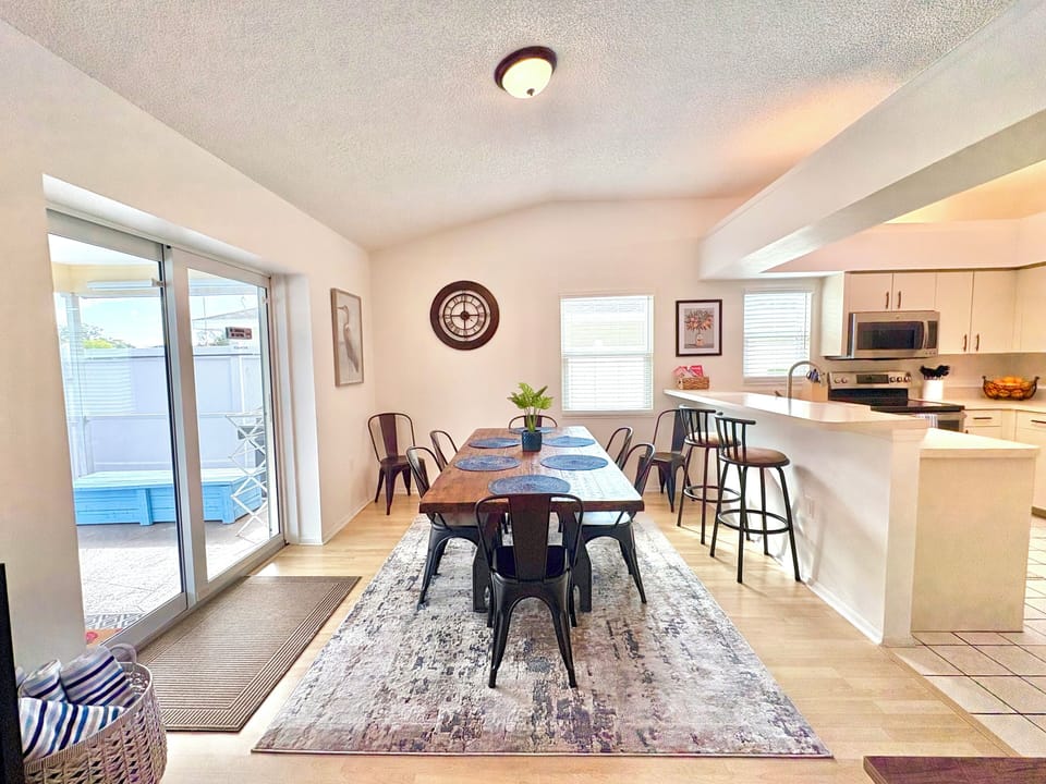 Open-plan dining and living area with wood table, bar seating, and sliding glass doors to pool