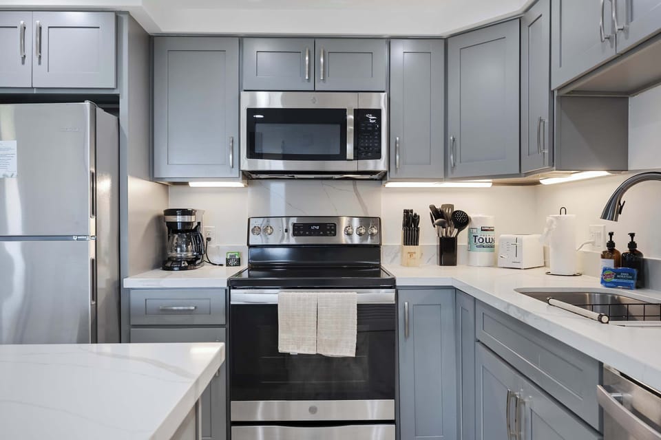 Whip up your favorite meals with ease in this modern, fully equipped kitchen featuring sleek stainless steel appliances, ample counter space, and grey cabinetry.