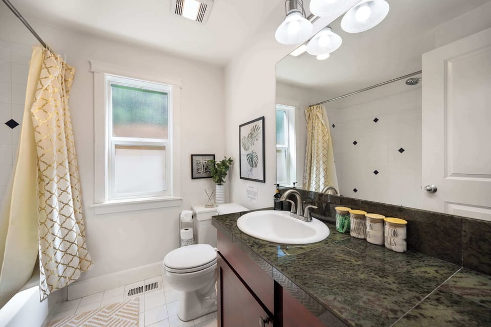Bright bathroom with granite counters, tub/shower combo, and cheerful yellow accents.