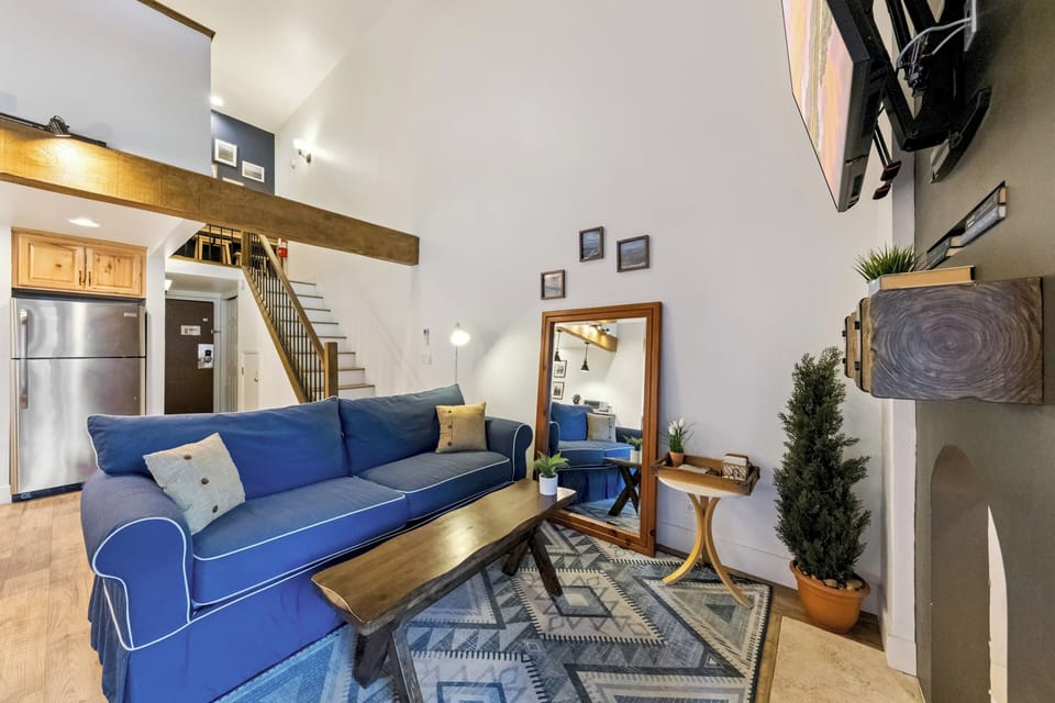 Your airy loft features soaring ceilings, exposed beams, and a vibrant blue sofa perfect for relaxing after city adventures.