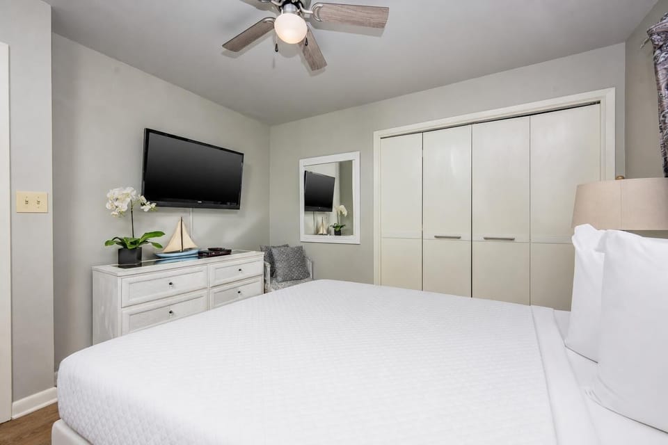 Guest bedroom featuring a plush white queen bed, a wall-mounted TV, and stylish decor for a relaxing getaway