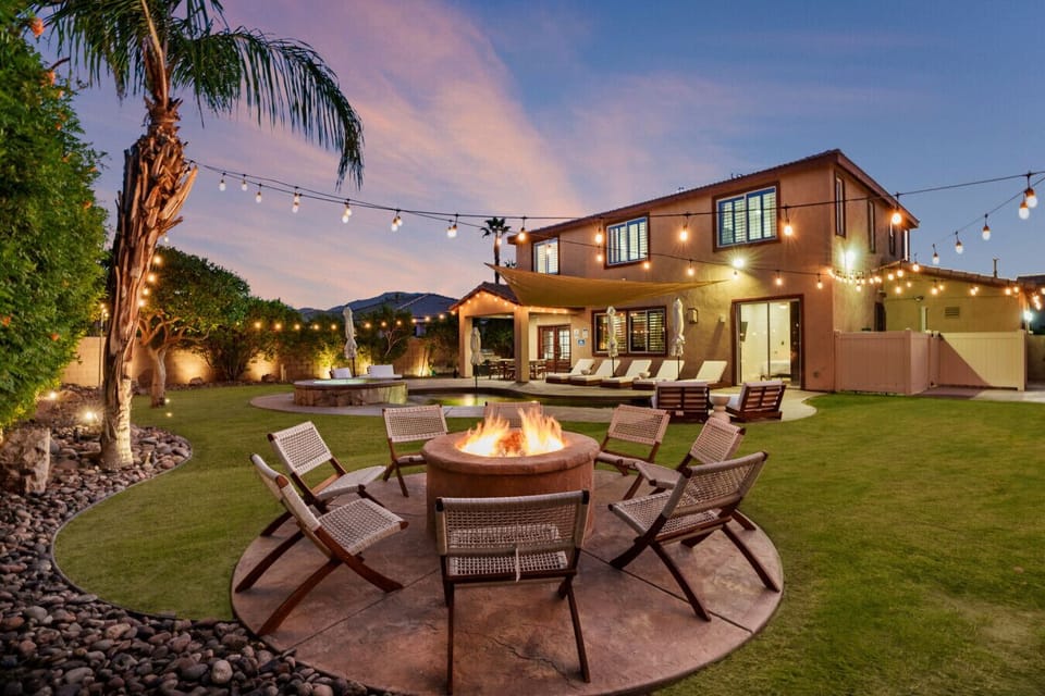 Backyard firepit lounge w/ string lights, cushioned chairs & twilight views for relaxed evenings under the sky.