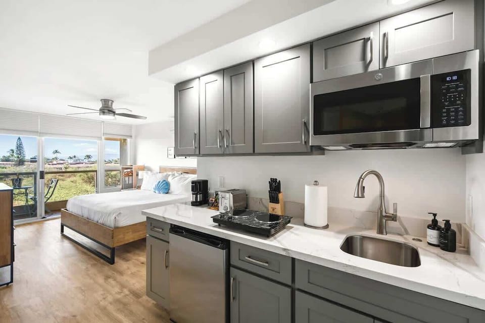Enjoy the ultimate convenience with a fully equipped kitchenette featuring a microwave and cooktop, all while looking out over your comfortable king bed toward the breathtaking partial ocean view from your private lanai.