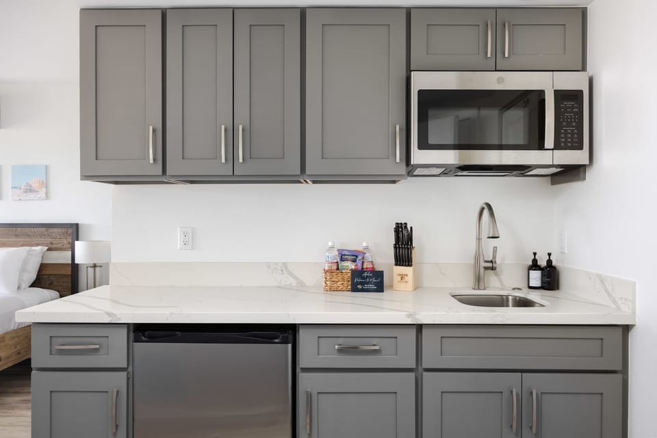 Prepare snacks and light meals with ease using this stylish kitchenette equipped with sleek gray cabinetry, modern stainless-steel appliances, and ample counter space.