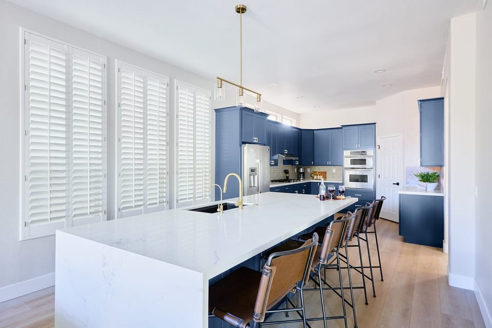 Stylish and functional kitchen with stainless steel appliances, navy cabinetry, marble countertops, and a spacious island with breakfast bar seating for 4.