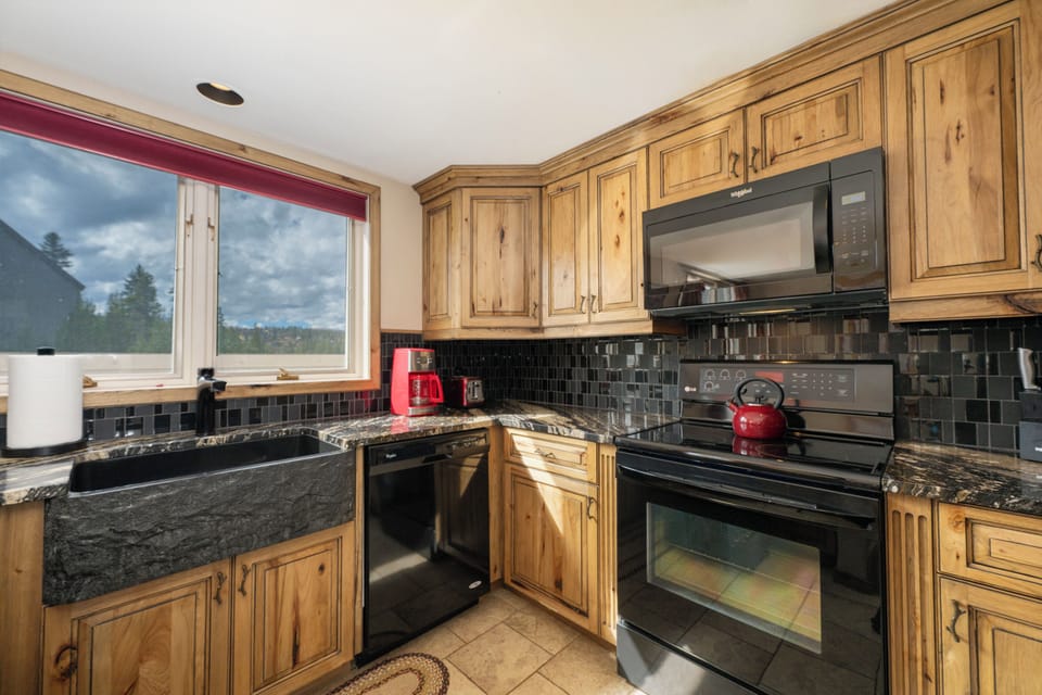 Your gourmet mountain kitchen awaits with rustic pine cabinets, granite counters, and a stunning forest view while you cook.