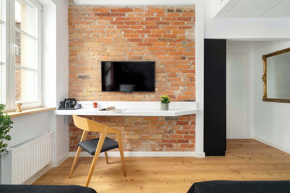 A furnished space for working at a desk. A flat-screen TV hangs on the wall with exposed brick.