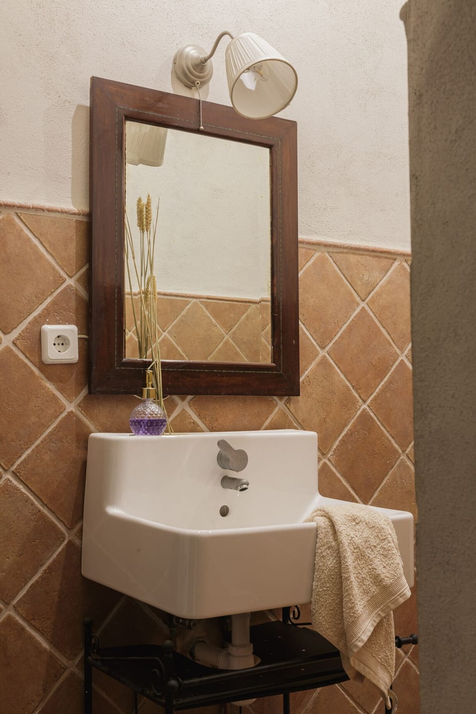 Bathroom detail with corner sink, wooden-framed mirror, wall sconce and diamond ceramic tiles; hand towel.