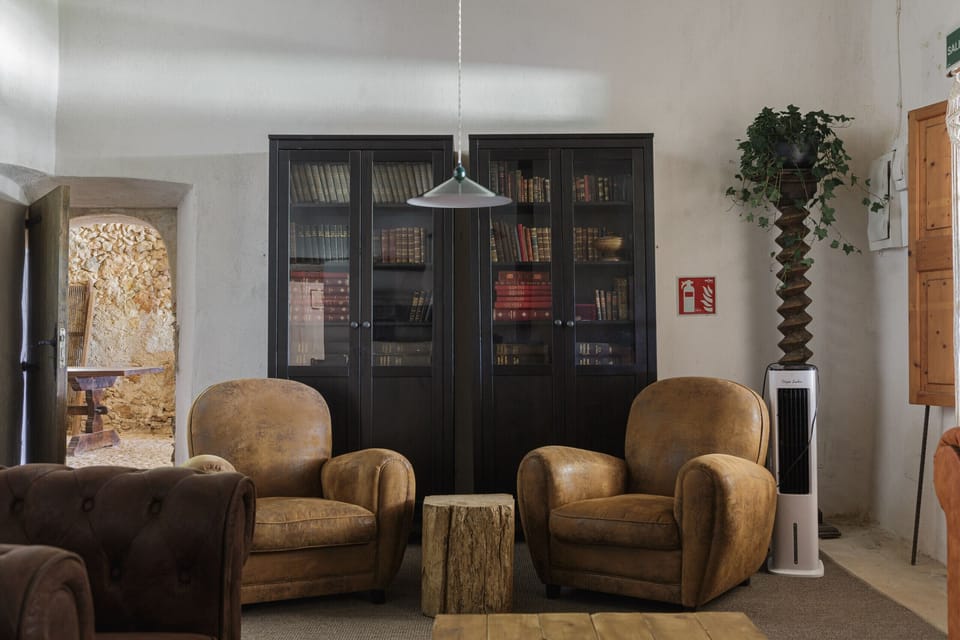 Cozy reading corner at Villa Sa Mata with leather armchairs, bookcase and rustic Mallorcan decor.