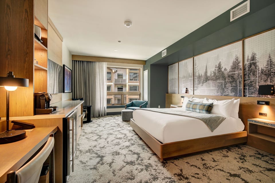 King bed with tree-mural headboard and sheer curtains framing a mountain-facing window