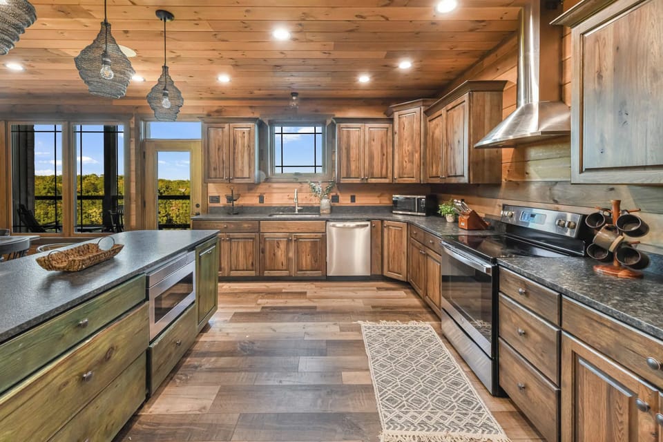 Rustic kitchen with wooden cabinetry and stainless steel appliances overlooking a scenic view.