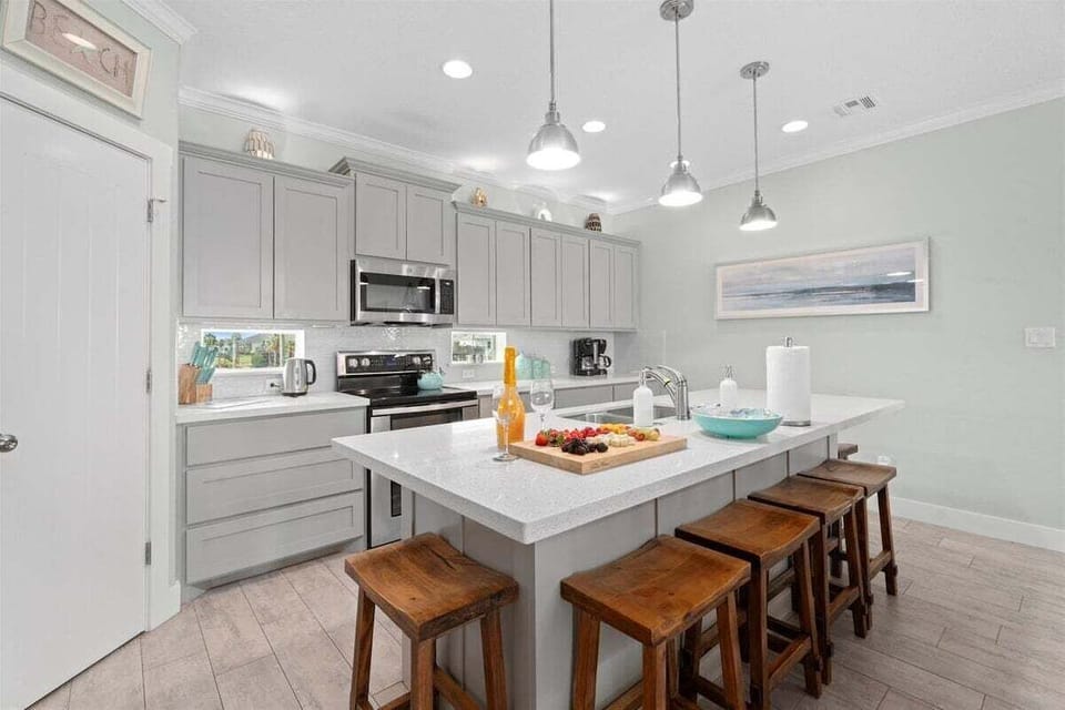 Spacious coastal kitchen with breakfast bar seating, quartz countertops, and stainless steel appliances.