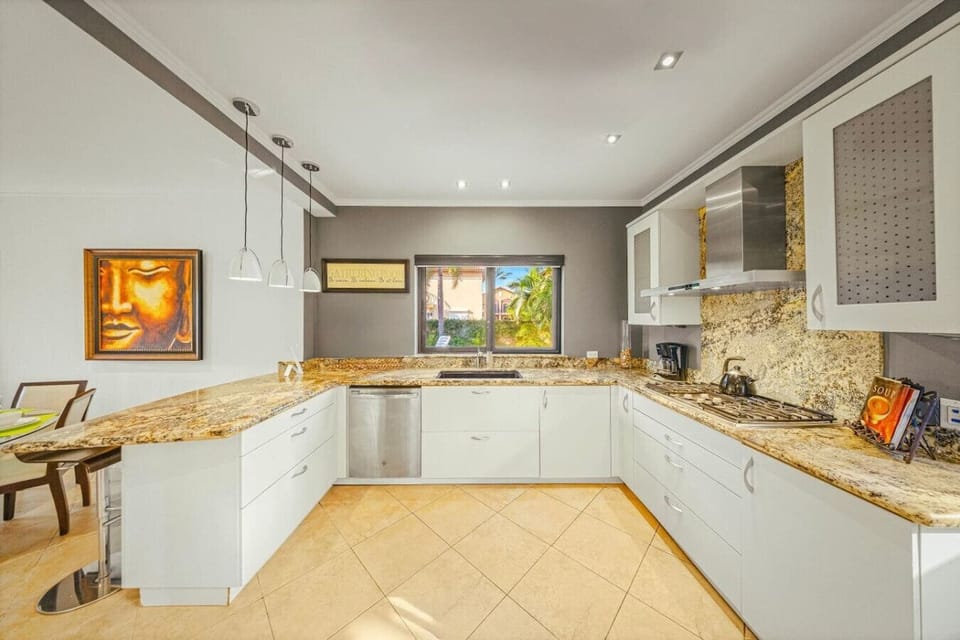 Golden granite counters, soft gray walls, and pendant lights create a refined, airy space ready for inspired cooking.