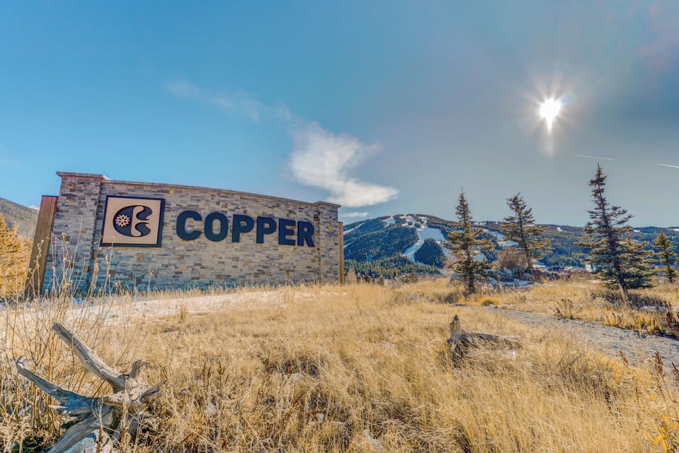 The Copper property entrance sign welcomes guests against a stunning mountain backdrop, with snow-dusted peaks and evergreen trees marking the arrival to this scenic mountain destination.