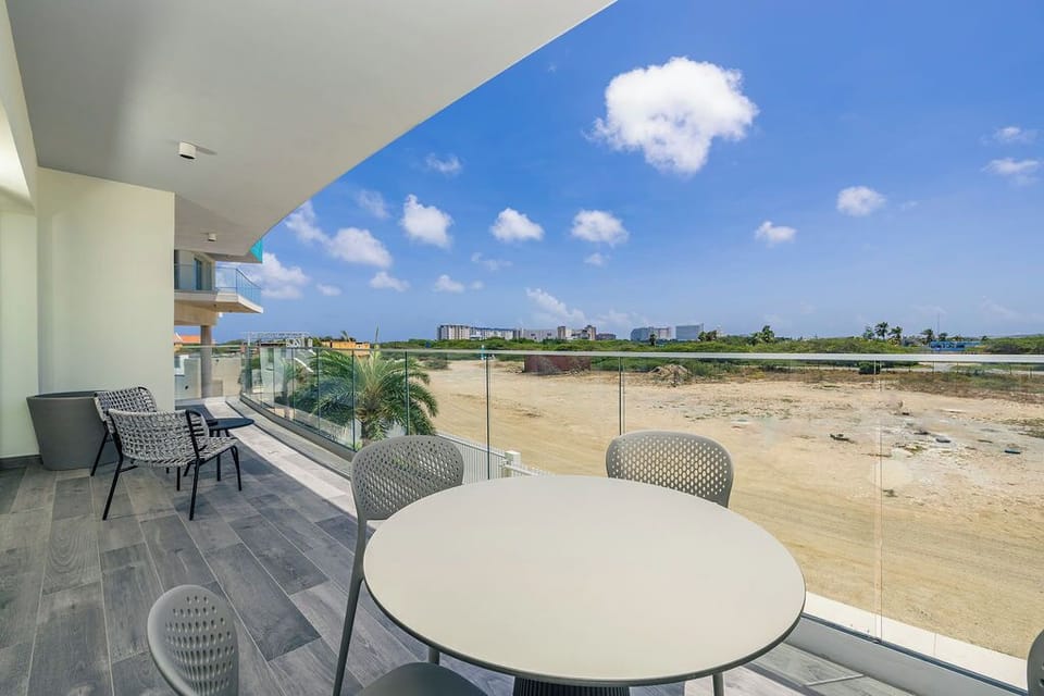 A modern balcony with glass railings and contemporary seating overlooks an undeveloped area. The property is located in a developing neighborhood with distant buildings visible on the horizon.