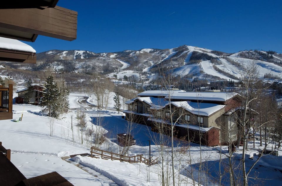 Mountain ski resort village nestled beneath snow-covered slopes with clear blue winter skies overhead.