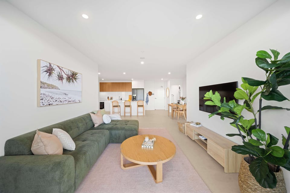 A spacious open-plan living area where a chaise sofa, wall-mounted smart TV, tranquil waterway outlook, and abundant natural light create a comfortable place to unwind.