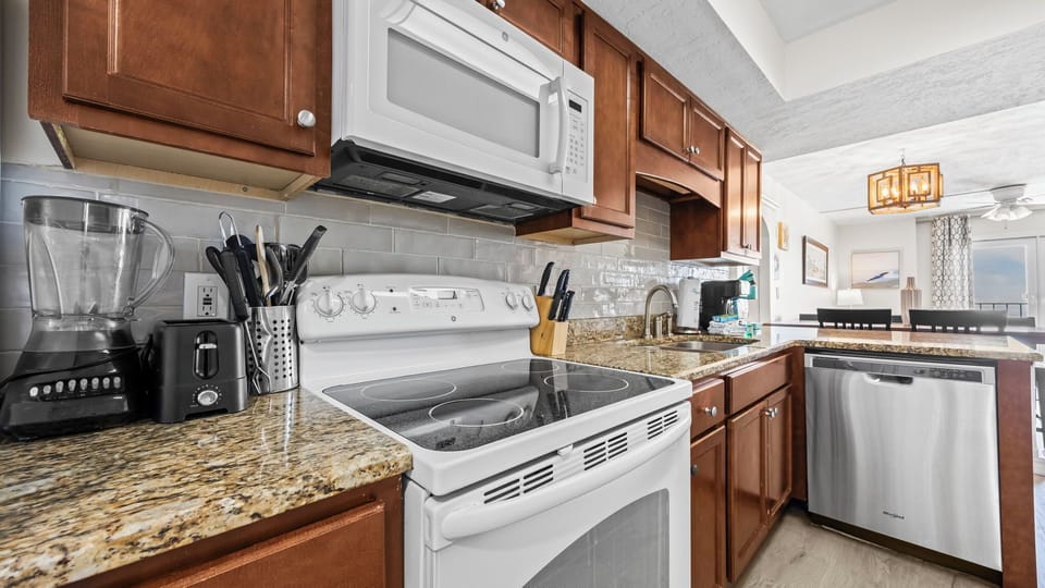 Surf Side Shores 1806 - Fully equipped kitchen featuring stainless steel appliances, breakfast counter with bar seating, and a seamless connection to the dining and living areas.