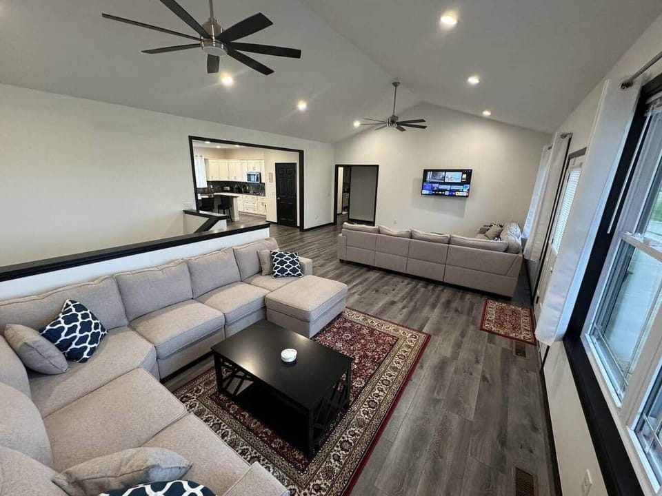 The living room features an LG 55" smart tv, 2 ceiling fans, two large sectional couches with rugs and coffee tables with drink coasters, and ample lighting.