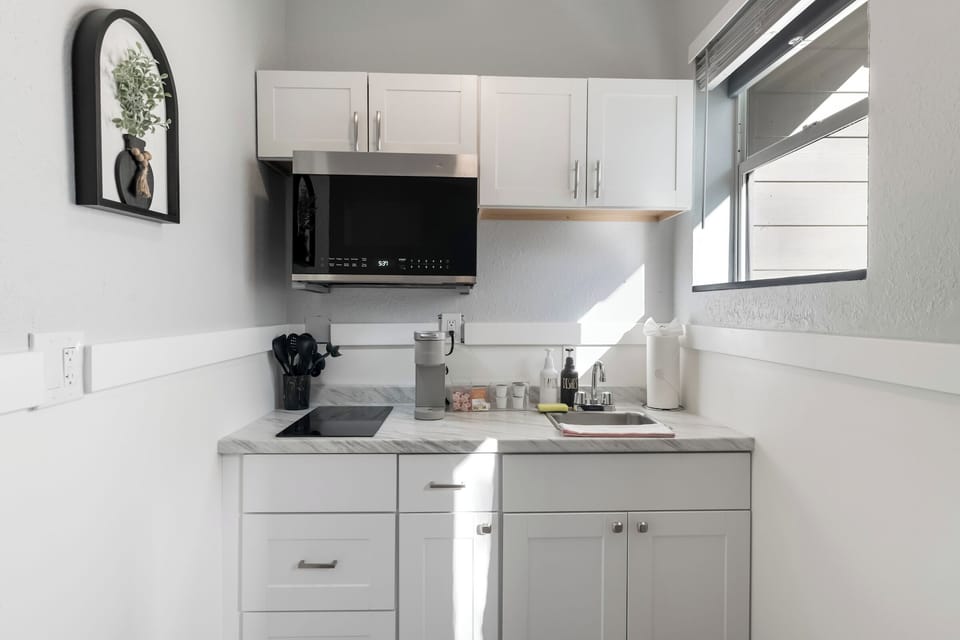 Compact white kitchen with sink, microwave, and coffee maker.