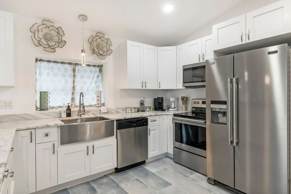 Modern white kitchen with stainless appliances and ample light.
