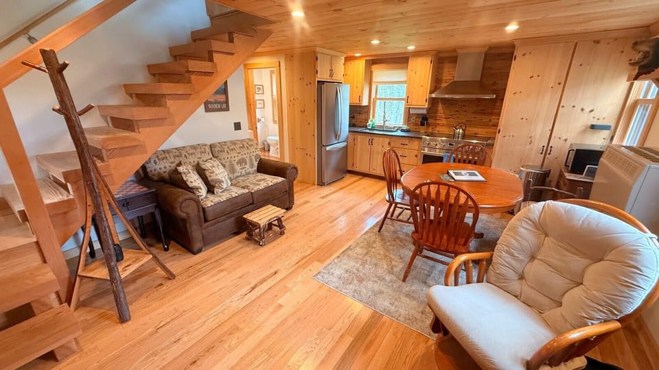 Cozy open-concept cabin featuring a fully equipped kitchen, dining area, and comfortable living space with warm wood finishes throughout.