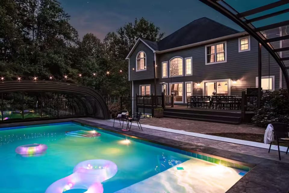Heated pool glows under string lights at the back of the home after dark